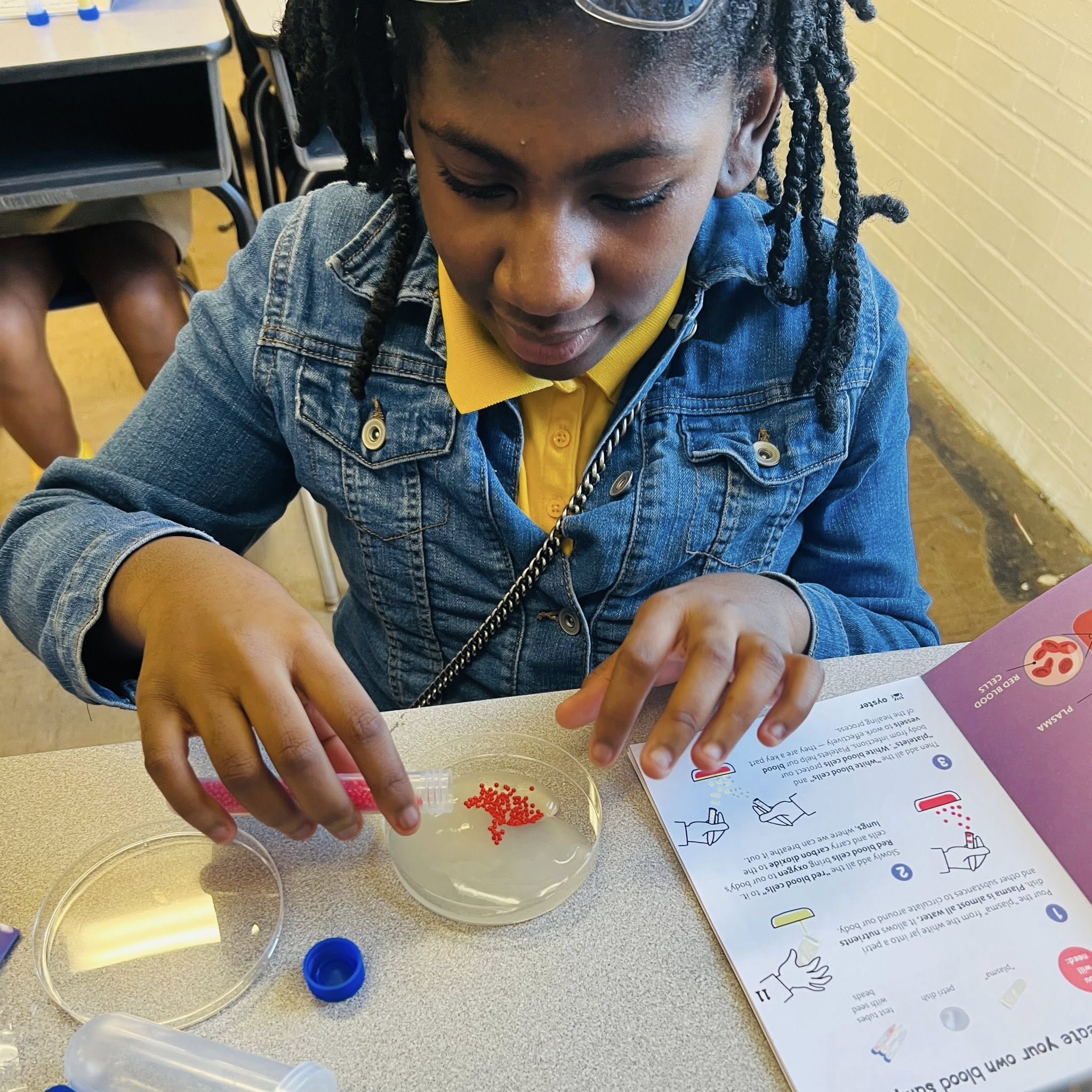 A girl pouring red beads into a petri dish.